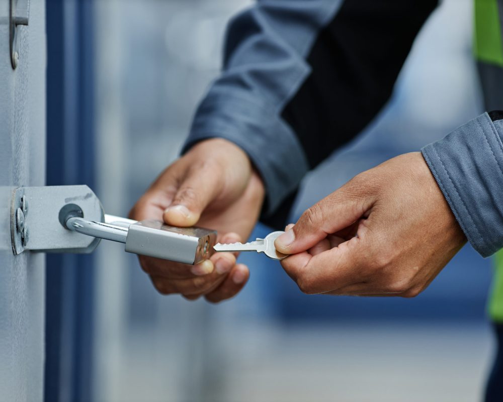 Close up of worker opening hanging lock with key on container door in shipping docks, copy space